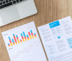 Un portatile di traverso con sotto alcune stampe che riguardano statistiche e marketing