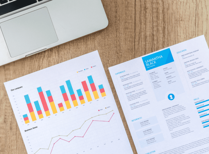 Un portatile di traverso con sotto alcune stampe che riguardano statistiche e marketing