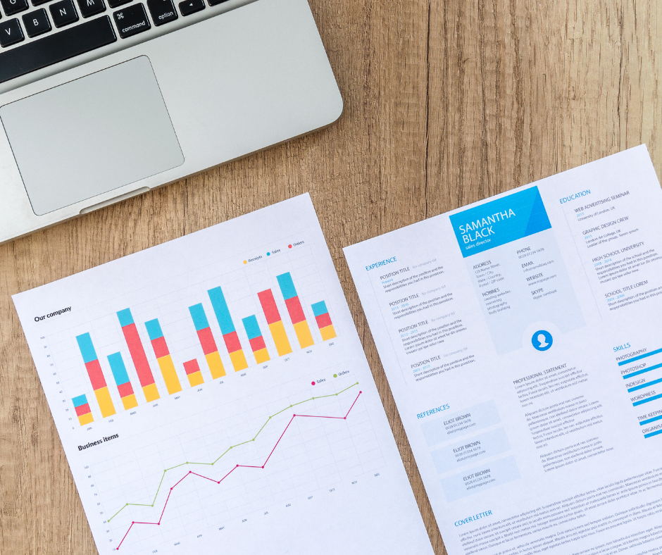 Un portatile di traverso con sotto alcune stampe che riguardano statistiche e marketing