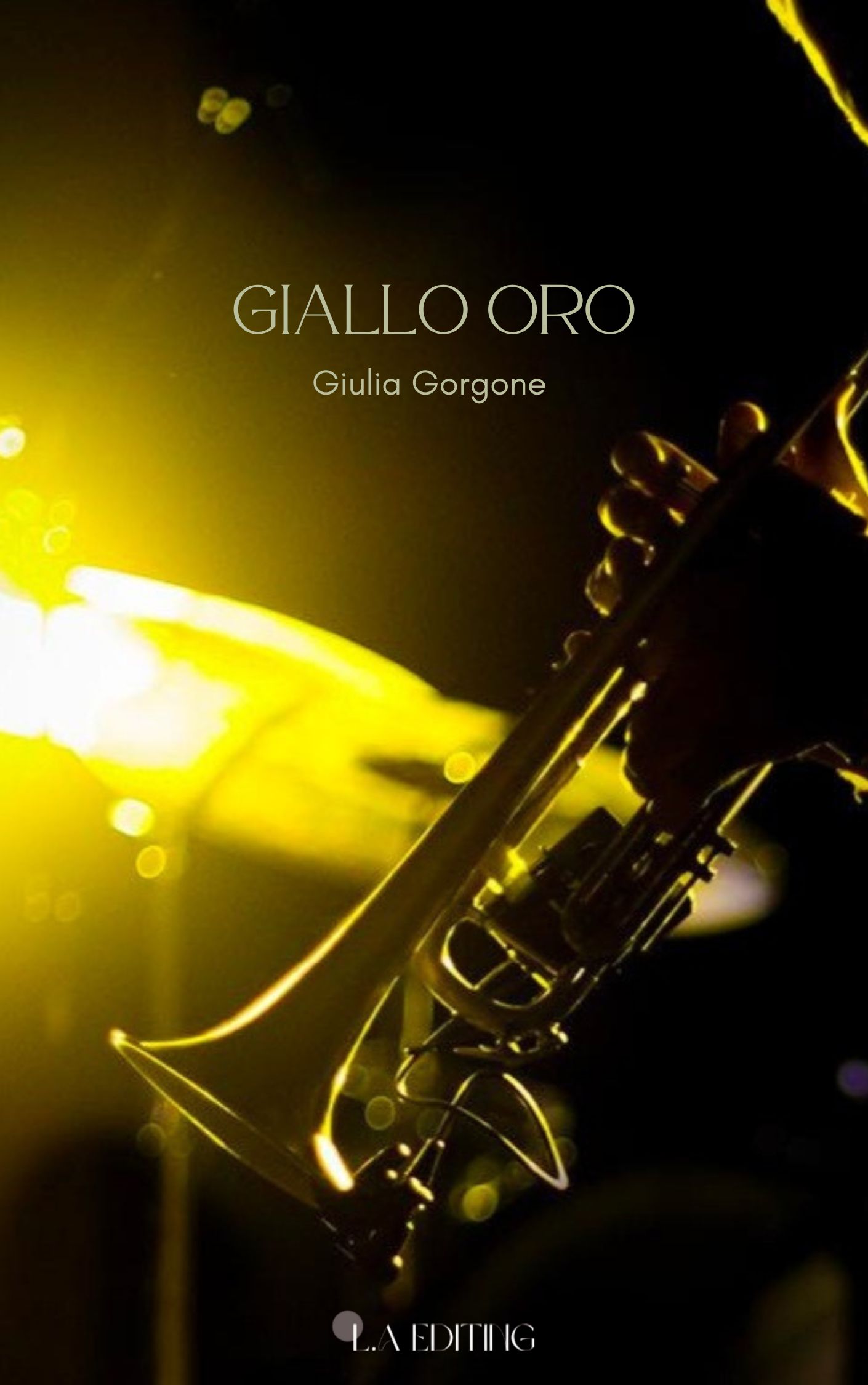 Copertina del libro "Giallo Oro" di Giulia Gorgone. L'immagine è una fotografia di Luca Ash in tonalità dorate, luci e ombre, che richiamano il giallo oro. Il soggetto è un uomo che suona la tromba, di cui si vedono solo le mani sui tasti. In evidenza c'è la tromba con un piatto della batteria alle spalle totalmente illuminato dalla luce dorata. Autrice del libro è Giulia Gorgone, format di pubblicazione in semi self publishing con L.A. Editing, progetto interno a L.A. Editing&Digital Marketing di Lara Aversano.